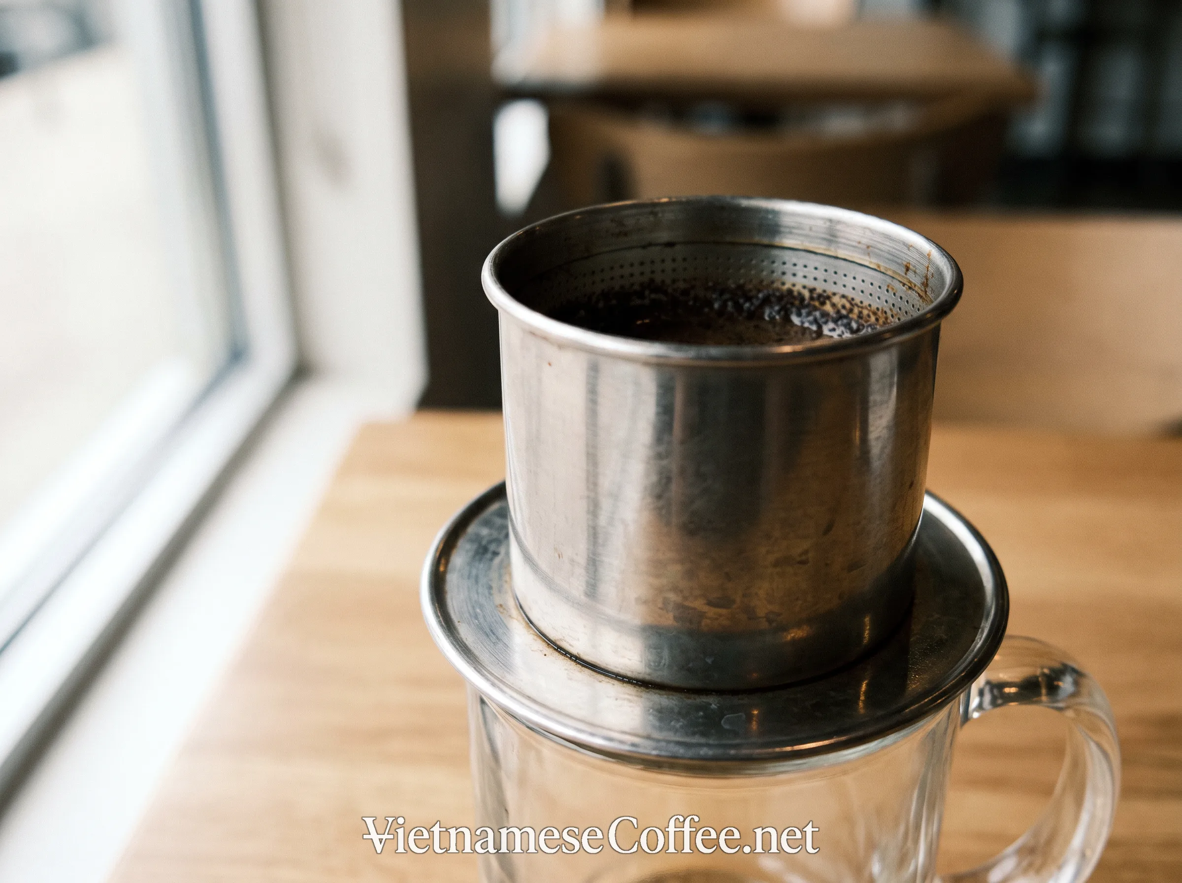 A phin filter dripping coffee slowly into a glass mug
