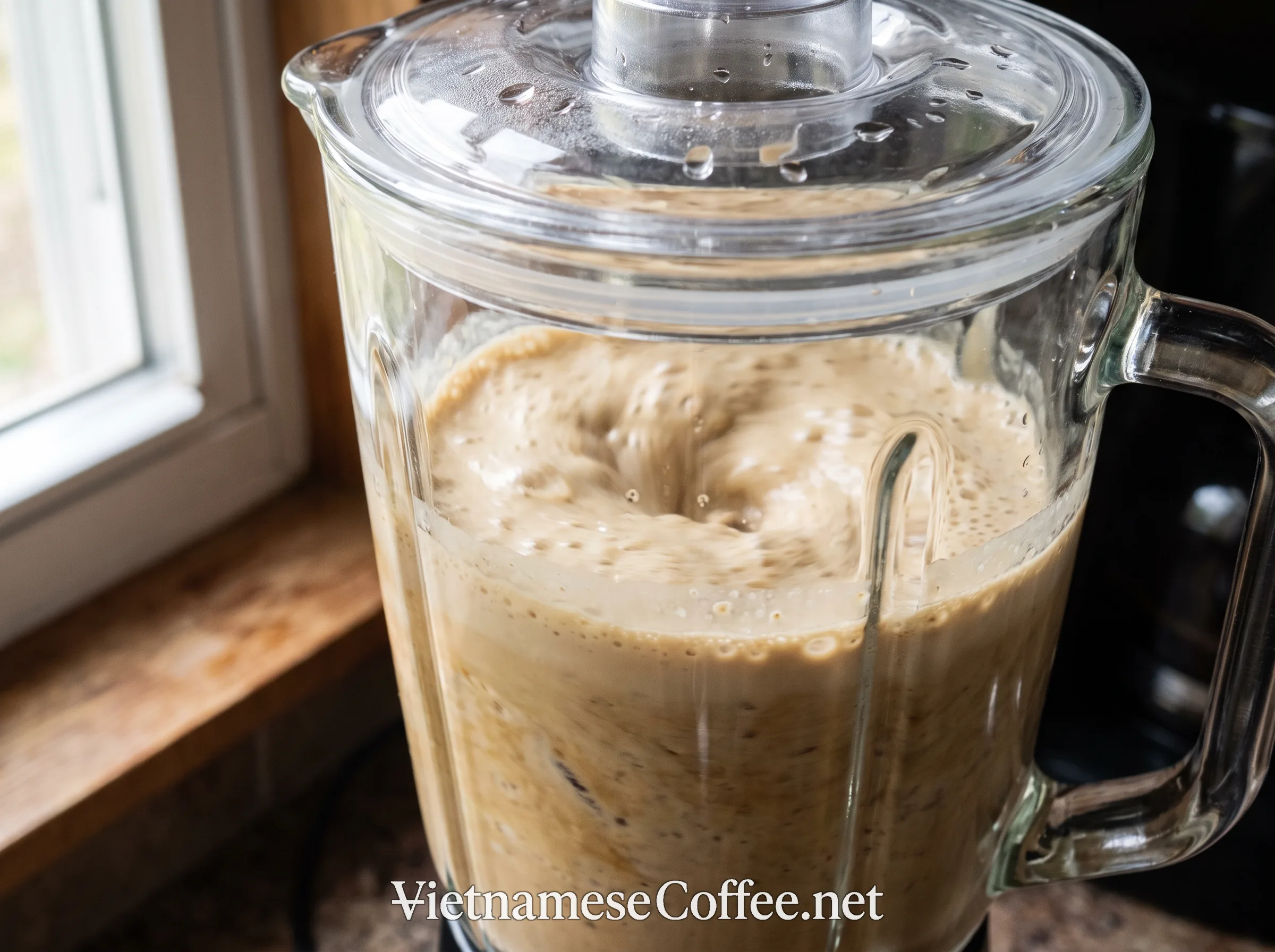 A pale brown coffee smoothie mid-blend in a blender jar