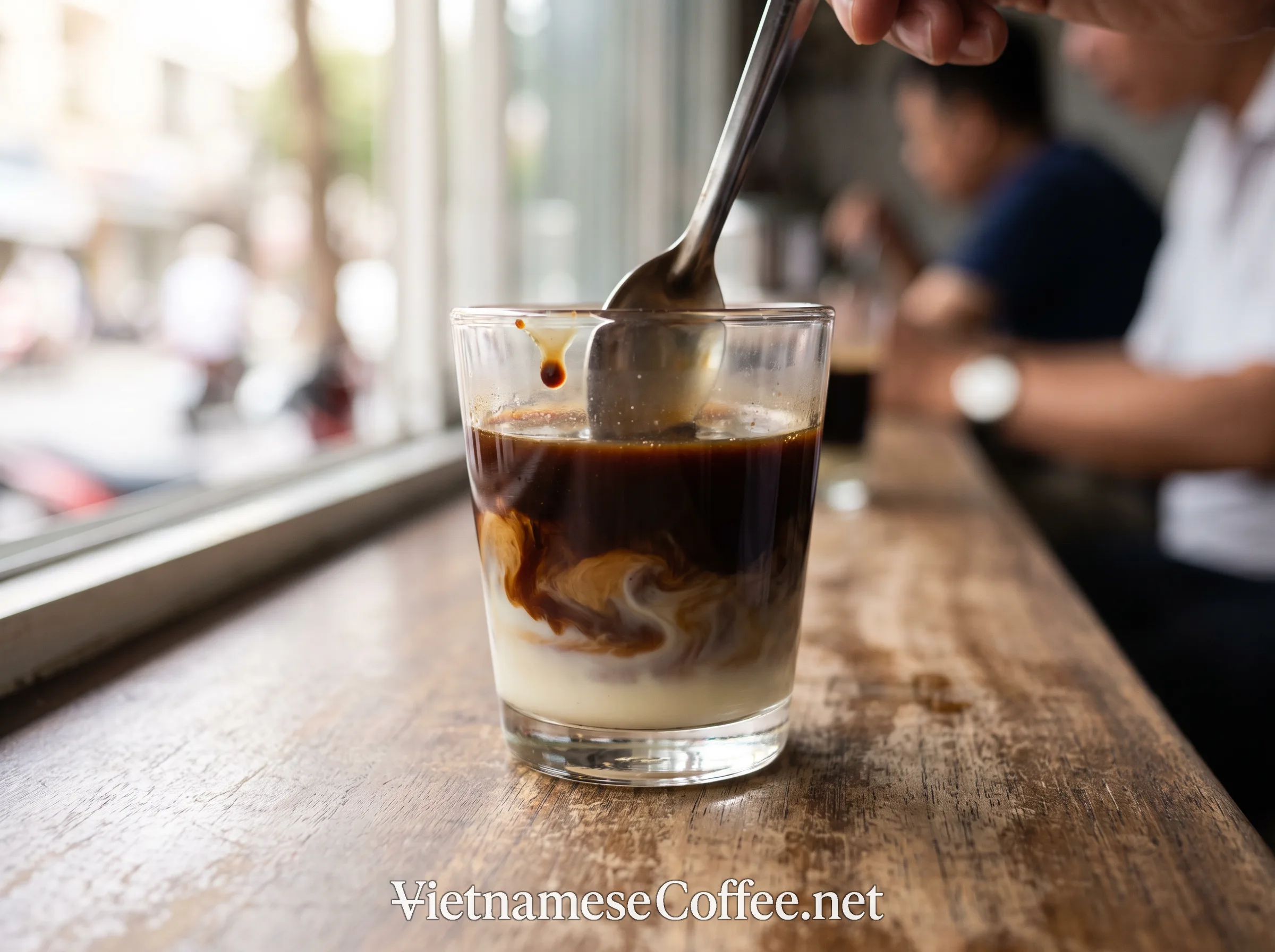 A spoon stirring coffee and condensed milk together in a glass before ice is added